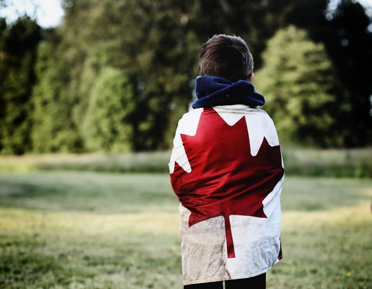 A person wearing a Canadian flag faces away from the camera and towards the treeline|Julie Greene smiles at the camera
