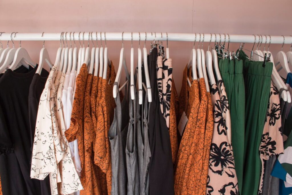 rail of earth-toned clothing against a pink wall