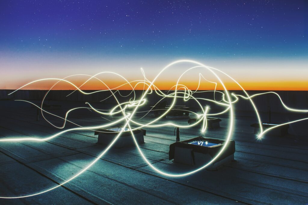 Twirling lines of electric light streak across a rooftop|Excited student using virtual reality goggles in the classroom.|Tech to Connect Logo - Tackling isolation through innovation|The three Tech to Connect Trophies