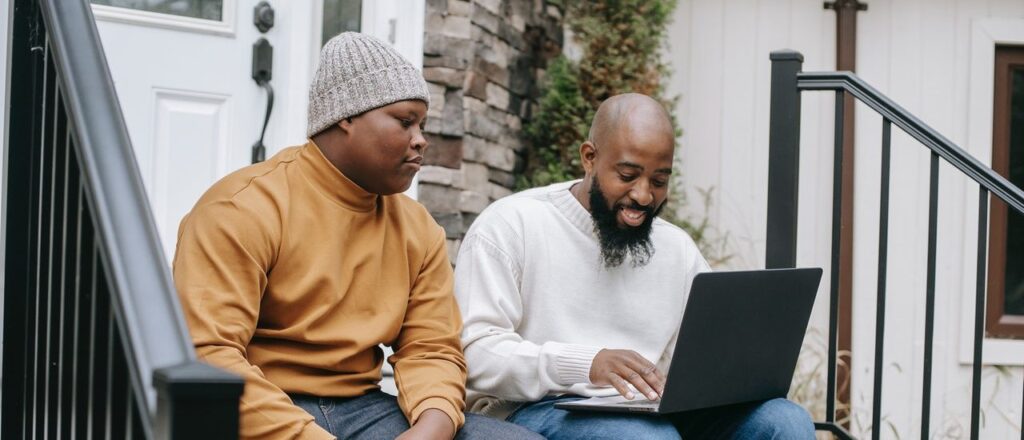 Two Black men sitting on steps in front of a house