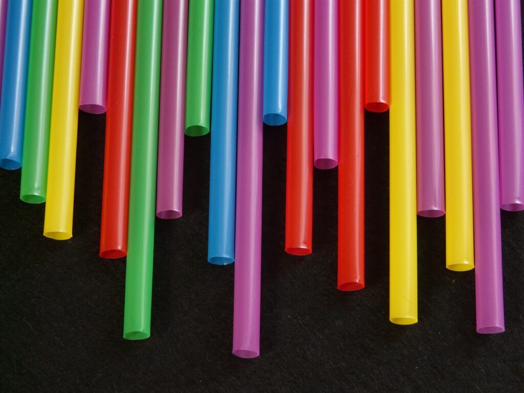 Coloured straws of different lengths are lined up to form an uneven curtain against a black background