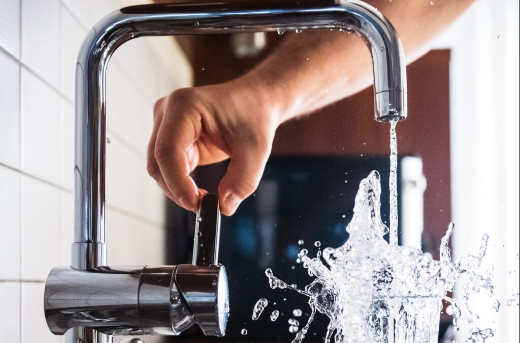 A white person's hand turning on a tap and filling up a glass of water