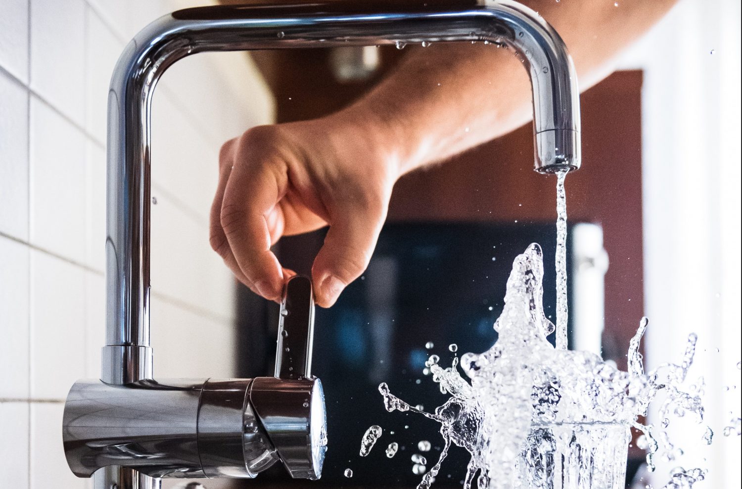 A white person's hand turning on a tap and filling up a glass of water