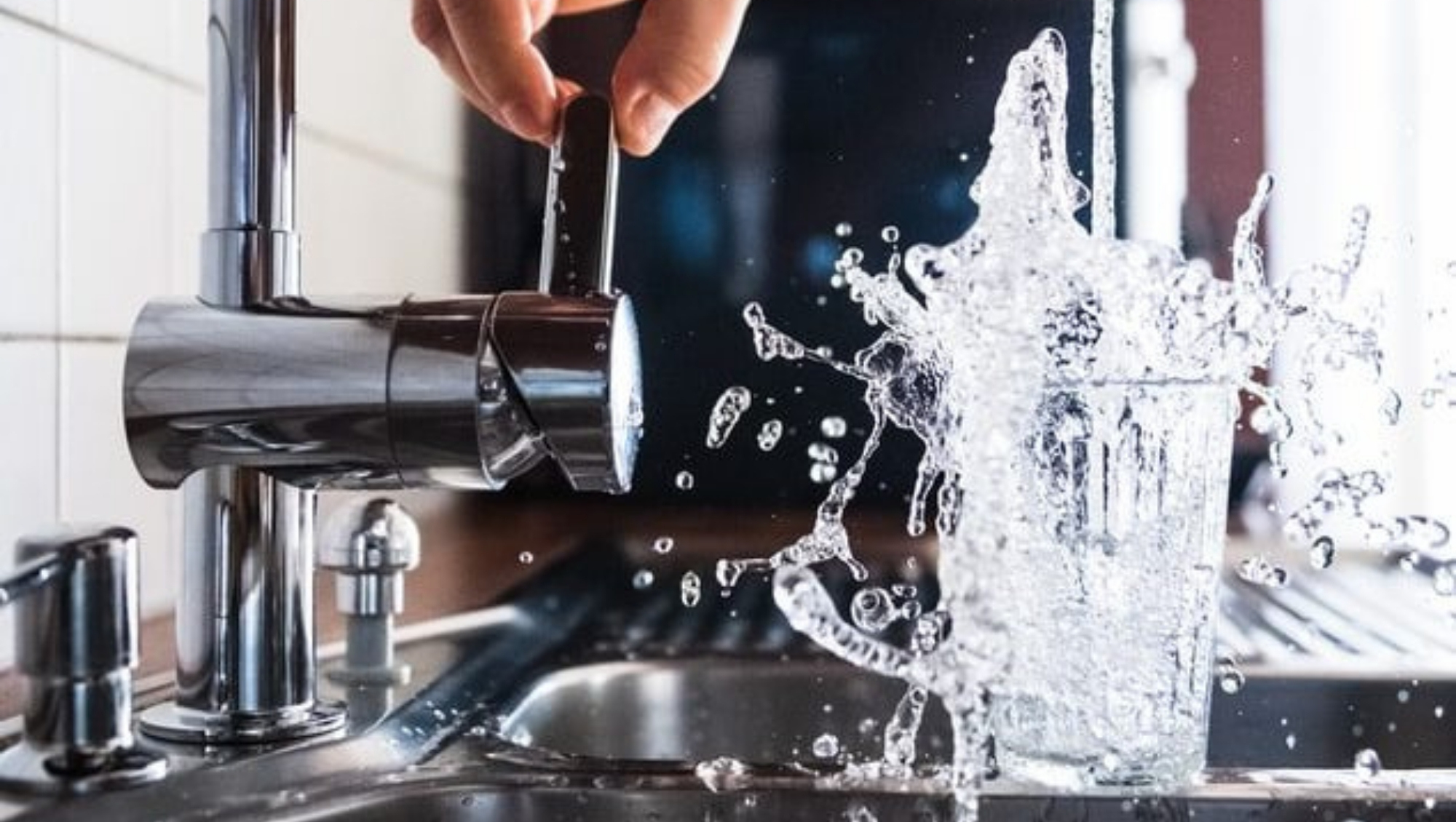 A hand turning a tap as fresh water splashes dramatically into a tumbler glass|