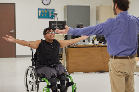 A wheelchair user reaches their arms out in a physiotherapy session|Toyota Mobility Foundation logo