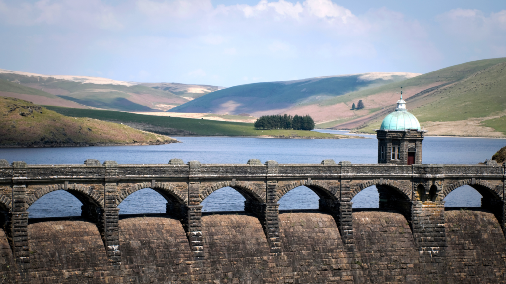 stone bridge going over a river with green hills in the background