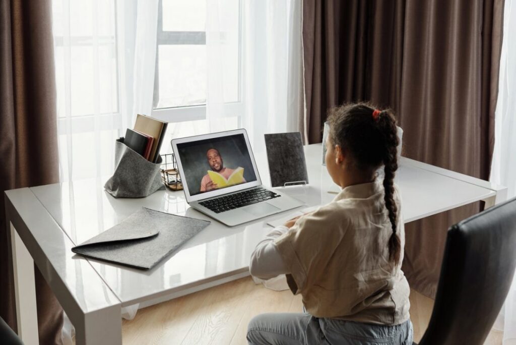 Young Black girl sat at a desk in front of a laptop. On the screen