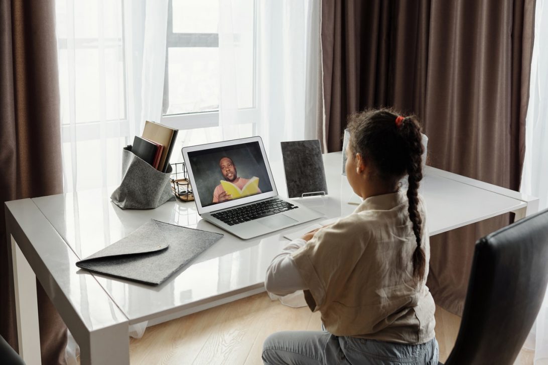 Young Black girl sat at a desk in front of a laptop. On the screen
