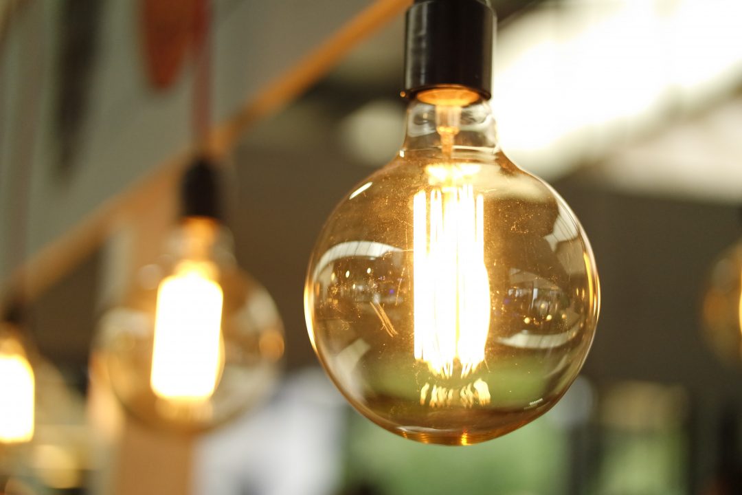 Close up of a warmly lit lightbulb|NPL logo - National Physical Laboratory|A group of people gathered around a yellow and white pull up banner for Hestia|NPL - National Physical Laboratory logo