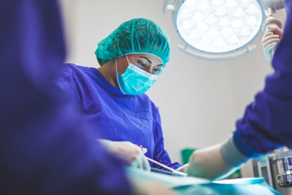 A surgeon in blue and purple scrubs performs surgery