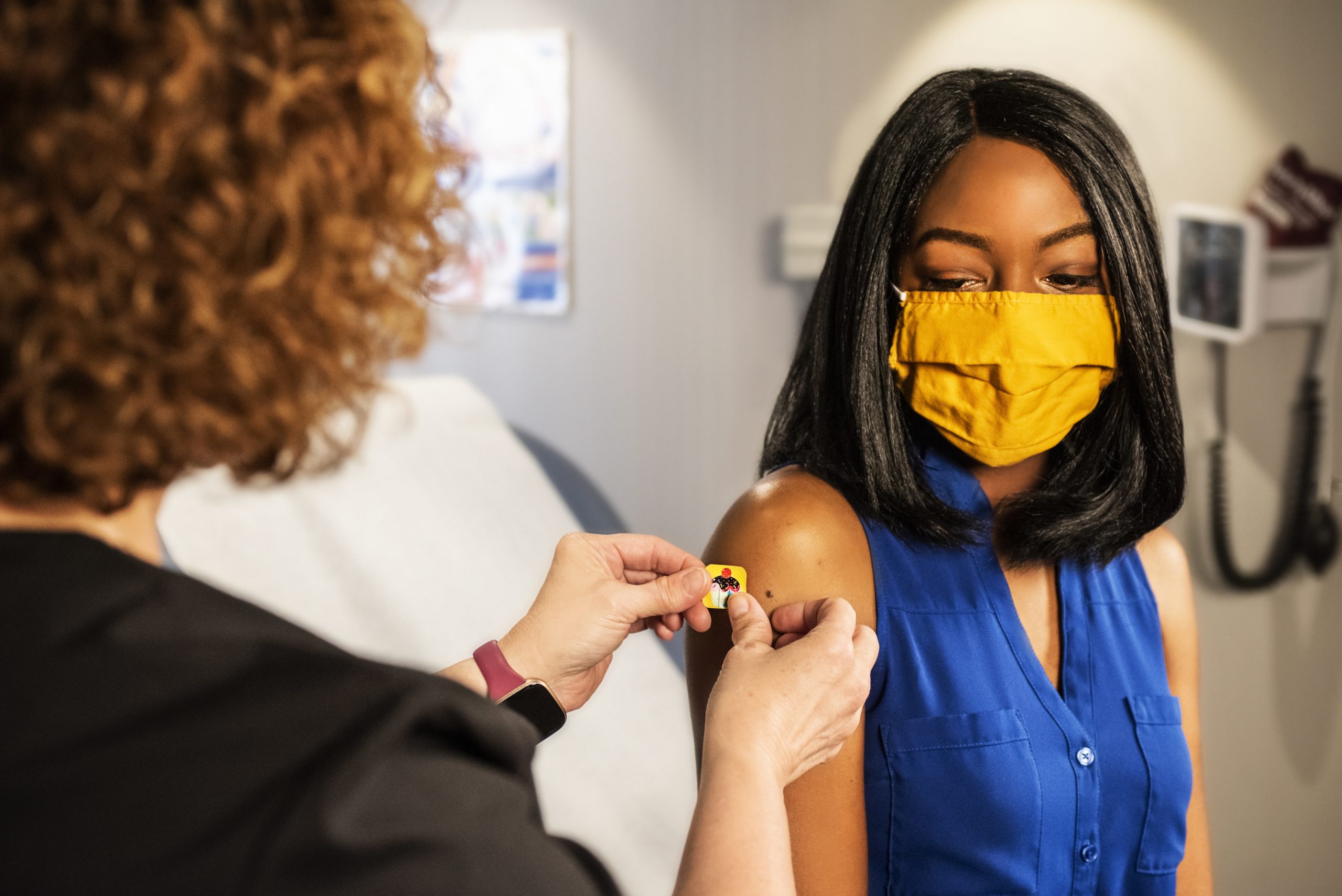 An image of a women wearing a mask getting a plaster put on her injection|An elderly man and woman at a table outside