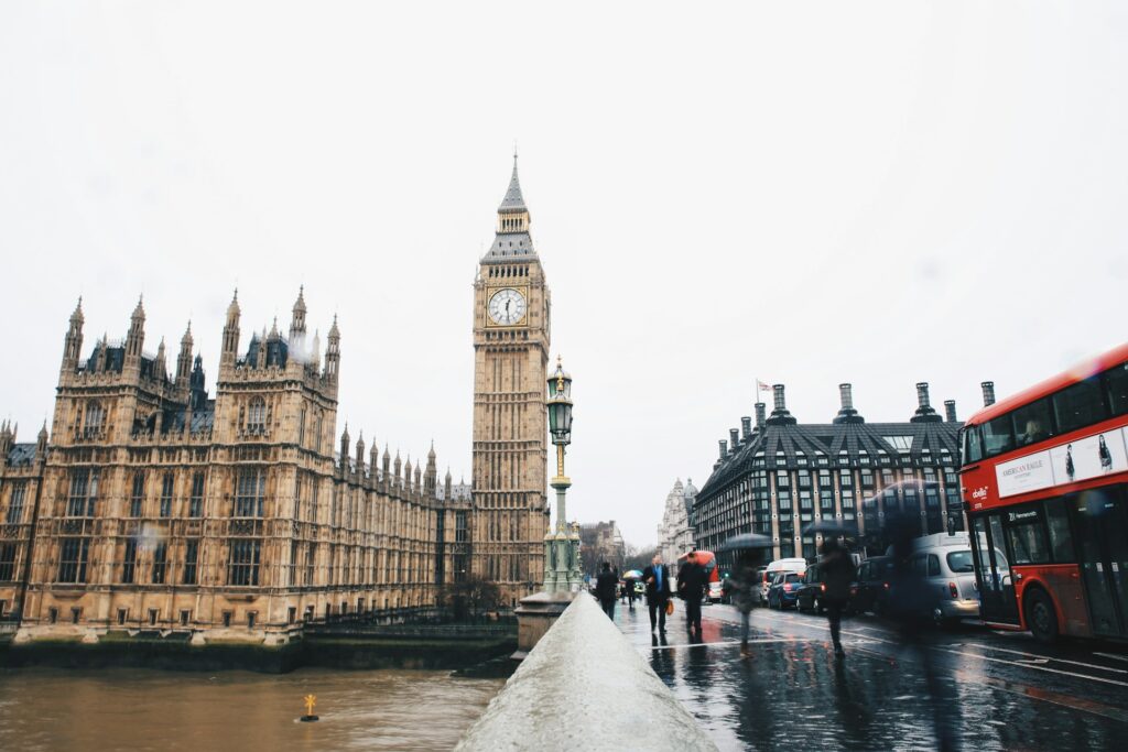 street photography of houses of parliament featuring a red double decker bus