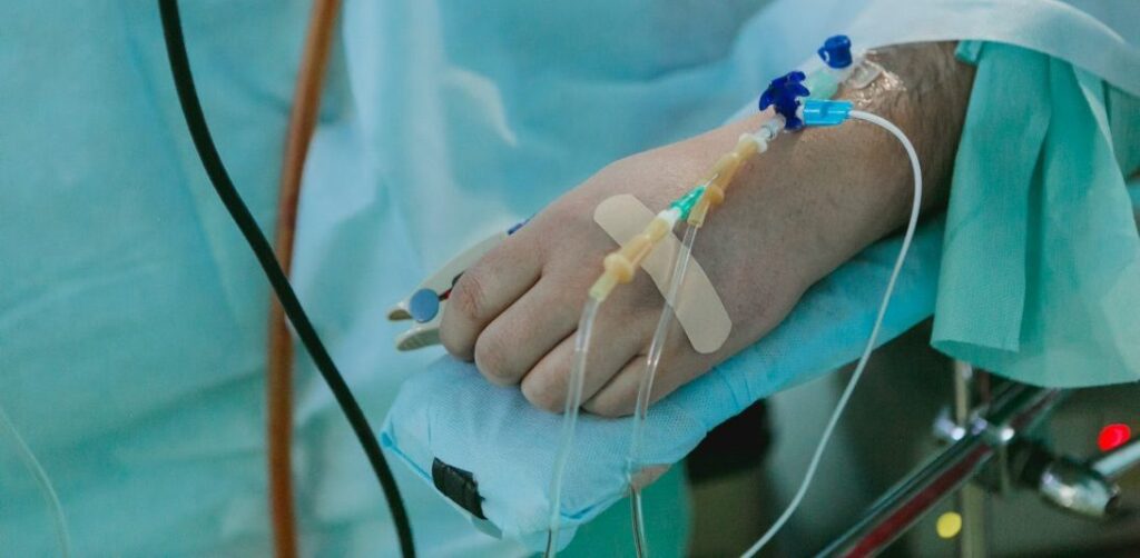 A hand with cannulas on an operating table covered with green sheets|Lady wearing full PPE and hijab answers phone with hand in a bright blue glove