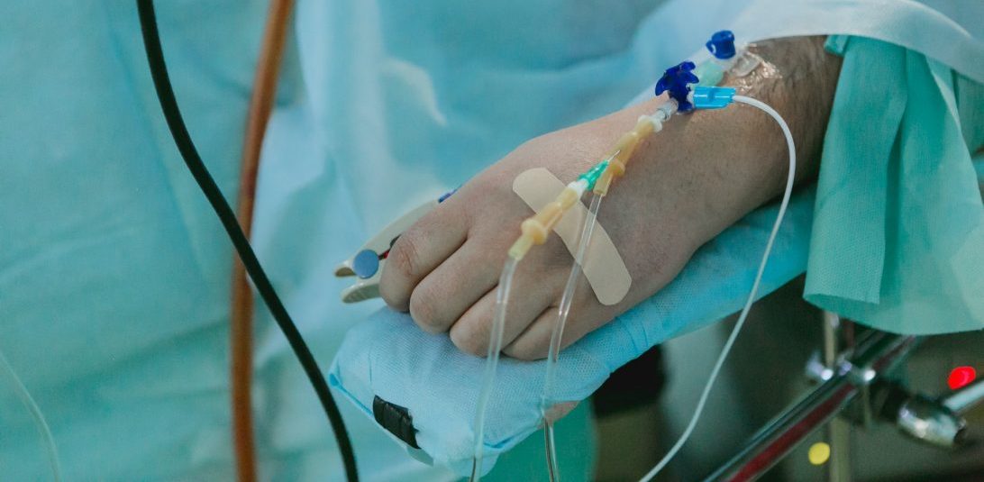 A hand with cannulas on an operating table covered with green sheets|Lady wearing full PPE and hijab answers phone with hand in a bright blue glove