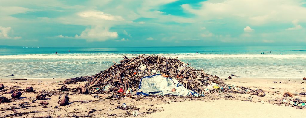 A pile of trash on the beach with blue water and sky.