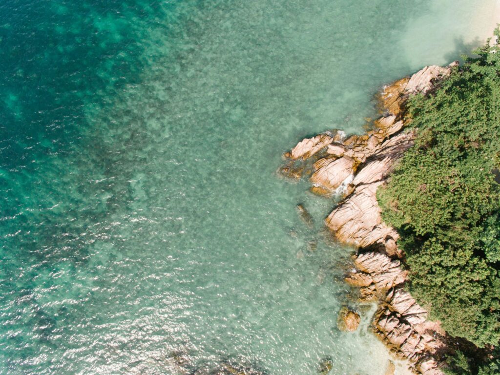 Ocean coast overhead|beach waves overhead|Image of a blue sea with rocks and a path for people to walk.|Image taken with a drone of a blue sea