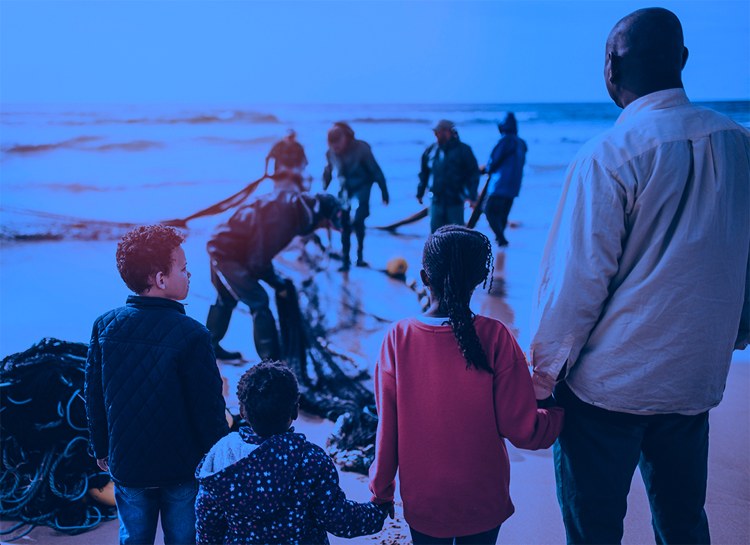Family standing on a beach|Three men gather round a woodworking project|Three people stand on a stage