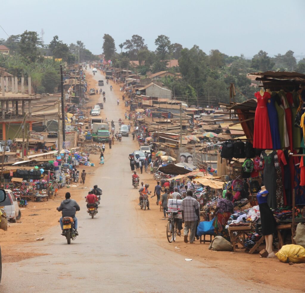 A busy dirt road with motor bikes and people on the side selling items of clothing