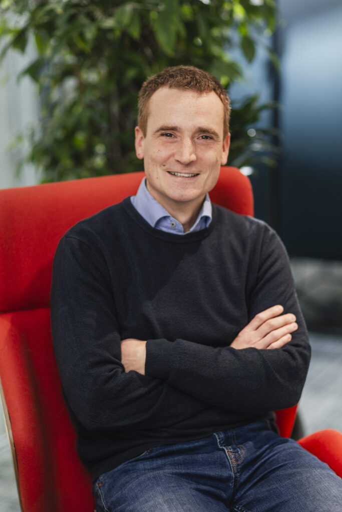 Photo of a white man sitting with his arms folded in a red chair